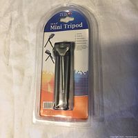 Front view of one Zeikos Mini Tripod in original sealed blister packaging with colorful pixel gradient background and Zeikos branding.