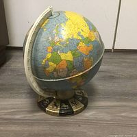 Photo of a vintage tin world globe showing Europe and Africa, mounted on a metal base with decorative animal silhouette squares.