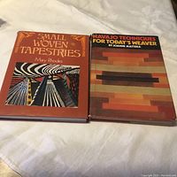 Photo of two hardcover weaving books lying side by side on a white surface. Left book titled "Small Woven Tapestries" by Mary Rhodes, right book titled "Navajo Techniques for Today's Weaver" by Joanne Mattera.