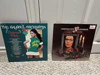 Front jackets of both Christmas LPs leaning against wall on carpeted floor