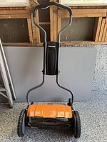 Front view of Fiskars StaySharp reel mower showing handle, frame, orange reel cover and wheels