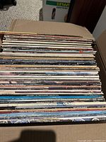 Stack of approximately 60 vinyl LP records inside a box, showing edge spines