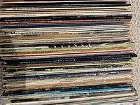 Stack of approximately 65 vintage LP records viewed from edge showing various titles