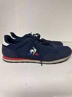 Side view of navy Le Coq Sportif sneakers showing tricolour logo and red midsole stripe
