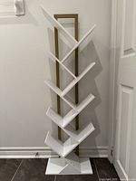 Full view of freestanding tree-style bookcase showing nine white angled shelves and gold frame