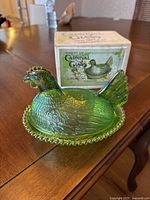 Iridescent lime green carnival glass hen with original box on table.