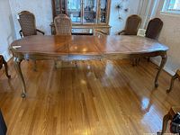 Full view of extended dining table with two leaves inserted, showing the polished wood surface and curved ornamental legs.