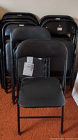 Front view of 14 stacked black folding chairs with one chair in front showing plastic upholstery and metal frame.