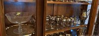 Glass fruit bowl on a pedestal, silver plate goblets and tray behind in cabinet shelf