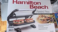 Box packaging front showing Hamilton Beach Panini Press and grilled sandwich images.