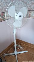 Full view of the white Hampton Bay floor fan standing on floor, showing height, base, cord, and grill with blades inside