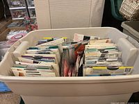 Large beige plastic bin filled with multiple packages of pantyhose and knee-high hosiery, organized upright.