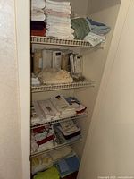Full view of linen cupboard shelving filled with assorted folded towels, packaged curtain panels and valances, tea towels, and sheets.