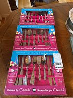 Three sealed boxed sets of Oneida stainless steel flatware displayed on wooden table