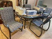 Full view showing table with various household items on top, four matching chairs with floral-patterned cushions around the table, and two loose cushions on one of the chairs.