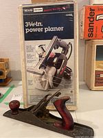 Photo showing Sears Craftsman power planer box and vintage hand planer on table.