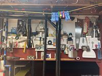 Wall-mounted red rack holding multiple hand tools such as saws, hammers, clamps, dustpans, measuring tapes, ropes, and sponges.