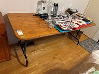 Full view of wood top utility table with various household items placed on top, table set on wooden floor.