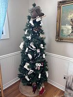Photo of a 6-foot green pencil Christmas tree decorated with multiple figure skating ice skate ornaments in white, brown, and black. The base is wrapped with a brown fabric tree skirt.