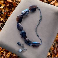 Set showing large faceted beads in amber brown with golden specks necklace laid out with matching pendant stone earrings on a beige background.