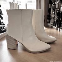 Pair of white faux leather women's ankle boots standing upright on a wooden surface showing profile view with chunky stacked heels.
