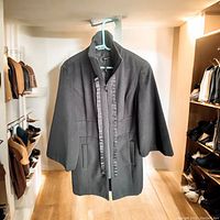 Full front view of the black dress coat showing mid-length cut, 3/4 sleeves, and ruffle detailing along the zipper.