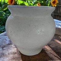 Large white clay heavy vessel with textured surface on wood table outdoors, sunlight highlighting finish and form.