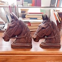 Pair of resin horse head bookends shown front and side views on a wooden surface with books in the background.