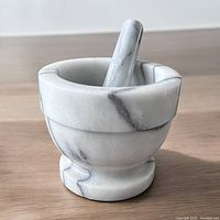 Mortar and pestle side view on wooden surface showing marble texture and design.