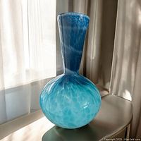 Side angle of a hand blown glass vase showing the bulbous blue swirled body and tall neck with a pontil mark at base.