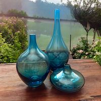 Three light turquoise art glass vases shown outdoors with garden background, illustrating color and shapes.