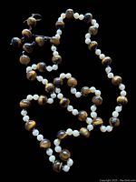Full view of necklace and pendant earrings against black background, showing alternating tiger eye and white pearl beads.