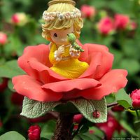 Front angled view of the Precious Moments figurine, showing girl in yellow dress sitting inside a large red rose with green leaves and a ladybug detail, holding a green caterpillar.