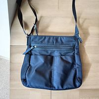 Front view of the black nylon crossbody Roots purse, showing two zippered compartments and adjustable shoulder strap.