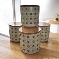 Four medium ceramic canisters stacked and grouped, showing top bamboo lids and yellow-green floral geometric pattern on the sides.