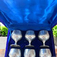 Open box showing three silver plated engraved egg cups standing upright on blue velvet interior