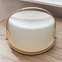 Full view of the Tupperware cake holder with white dome lid and golden yellow base with handle on top.