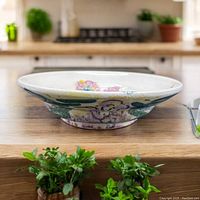 Side profile of the wide, shallow pottery bowl showing handpainted floral design around the exterior and interior with a cream base color.