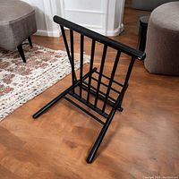 Black vintage wooden folding foot stool standing on a wooden floor, showing the front and base structure