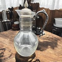 Full view of the vintage 1950s water carafe showing glass body and silver plated handle and lid with decorative finial.