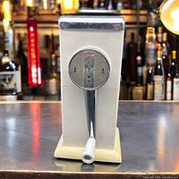 Front view of vintage Ice-O-Mat hand crank ice crusher in white with chrome details, showing the hand crank and dial.