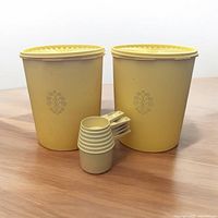Photo in natural lighting showing two yellow Tupperware cannisters with lids and four nested measuring cups on wooden surface.