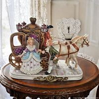 Full view of the porcelain Victorian horse drawn carriage figurine on a wooden table showing coachman, lady figure, gentleman figure, two horses, and detailed carriage.