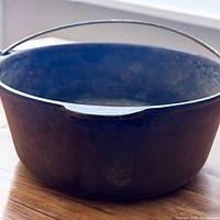 Front side view of the vintage Wagner cast iron pot showing the rounded rim and metal handle with patina.