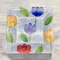 Top view of square serving dish showing colorful tulip pattern with green leaves on speckled background.