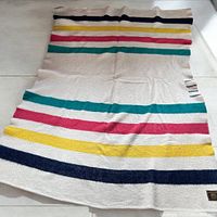 Full photo of the blanket spread out showing the classic Hudson's Bay five point stripe pattern with navy blue, yellow, red, and green stripes on a cream background.