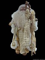 Full standing view of Santa Claus figure in cream and gold clothing holding staff and bag