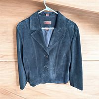 Front view of a black women's blazer made of suede with button-up front on hanger against wooden background.