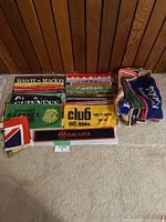 Overview of all vintage bar towels featuring diverse beer and soft drink logos arranged on floor against wooden paneling.