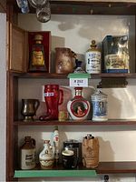 Front and right angled view of entire set of vintage bar bottles, showing box, jugs, steins, bottle shapes and colors on shelves